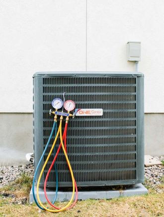 Air conditioning unit with gauges attached, featuring red, blue, and yellow hoses connected to it, likely during an AC installation in Magna, UT.